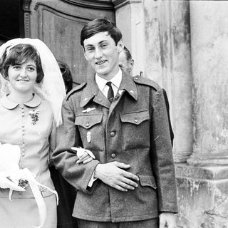 Couple in military uniform and wedding dress pose for photo.