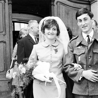 Couple in military uniform and wedding dress pose for photo.