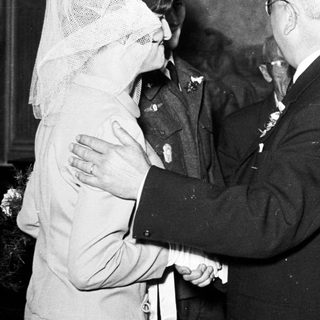 Man shakes hand with woman wearing a veil, group observing.