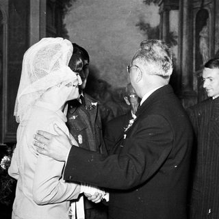 Man shakes hand with woman wearing a veil, group observing.