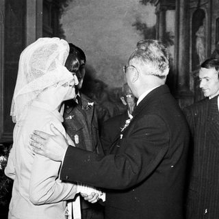 Man shakes hand with woman wearing a veil, group observing.