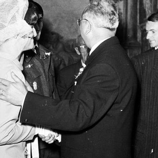 Man shakes hand with woman wearing a veil, group observing.