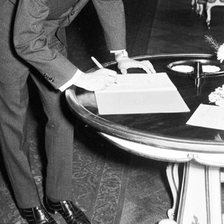 Man in suit signs document at a formal event.