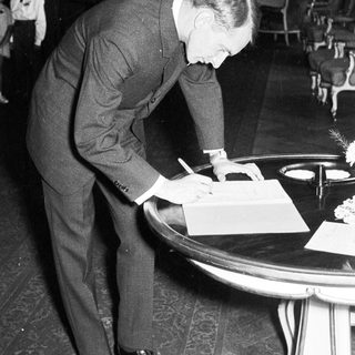 Man in suit signs document at a formal event.