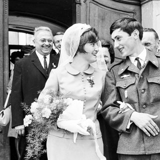 Bride and groom exiting a building, surrounded by guests.
