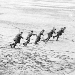 Here's a brief summary of the image: Troops and individuals in a barren, open landscape.