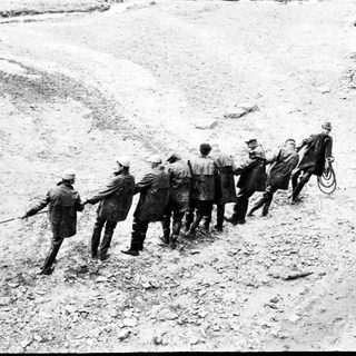 Men pull a rope across a rocky, barren landscape.