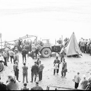 Group of people gather near vehicles and a tent.