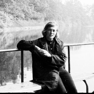 Man sitting near water, looking towards the trees.