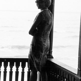 Two figures stand on a balcony overlooking the sea.