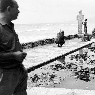 People overlooking a coastal scene with a memorial cross.