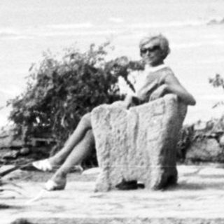 People overlooking a coastal scene with a memorial cross.