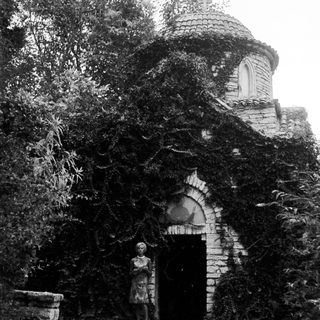 Overgrown, historic building with a woman standing in front.