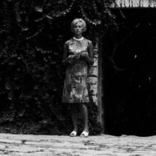 Overgrown, historic building with a woman standing in front.