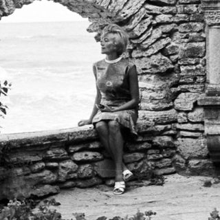 Here's a brief summary: Woman sits near a statue within a stone structure.