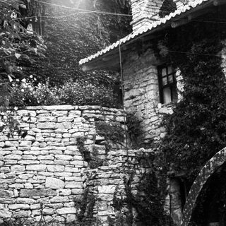 Stone wall, building, and archway covered in foliage.
