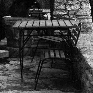 Man seated outdoors, stone wall and table visible.