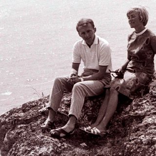 Couple seated on a rocky cliff overlooking the sea.