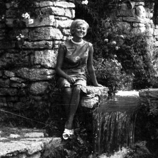 Woman sits near a waterfall in a stone garden.