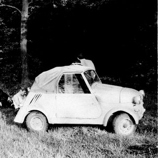 Vintage car and people stranded in a wooded area.