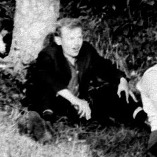 Vintage car and people stranded in a wooded area.