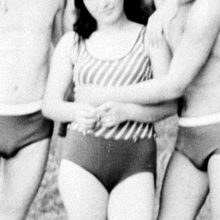 Four people posing near a lake in vintage swimwear.