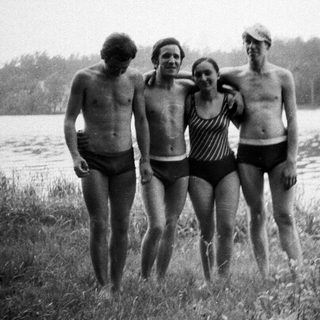 Four people in swimwear stand near a lake.