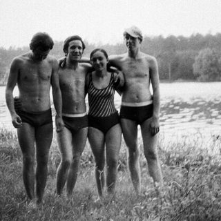 Four people in swimwear stand near a lake.