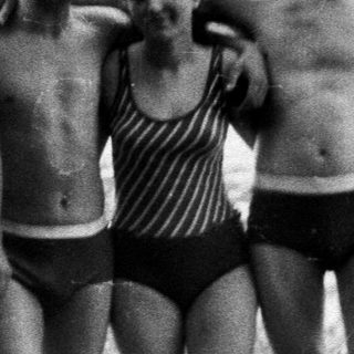 Four people in swimwear stand near a lake.