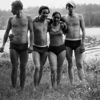 Four people in swimwear stand near a lake.