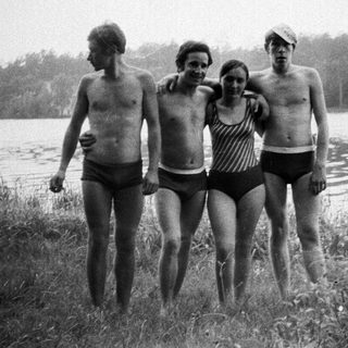 Four people in swimwear stand near a lake.