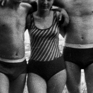 Four people in swimwear stand near a lake.