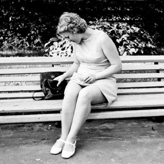 Woman sits on a bench, looking down, handbag nearby.