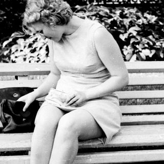 Woman sits on a bench, looking down, handbag nearby.