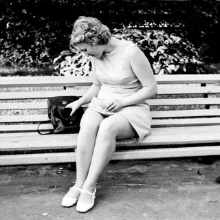 Woman sits on a bench, looking down, handbag nearby.
