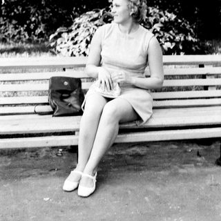 Woman seated on a park bench in a dress.