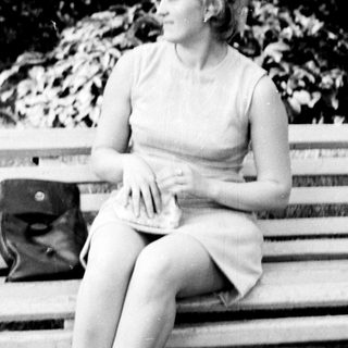 Woman seated on a park bench in a dress.