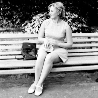Woman seated on a park bench in a dress.