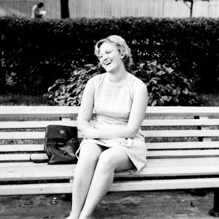 Woman laughs while seated on a park bench.