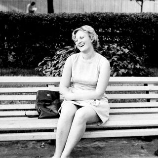 Woman laughs while seated on a park bench.