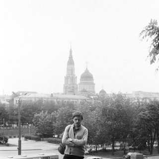 Man stands on a street with a large building in background.