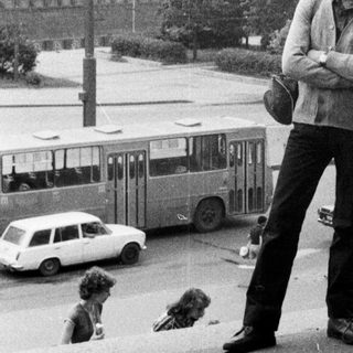 Man stands on a street with a large building in background.