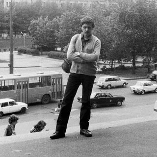 Man stands on a street with a large building in background.