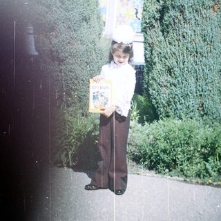Young girl holding book outside school building.