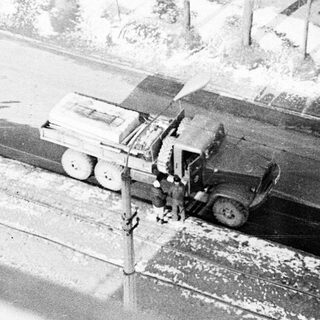 Military truck on snow-covered road near railway tracks.