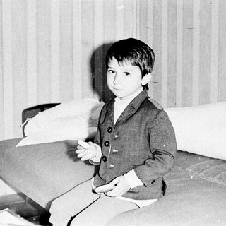 Young boy in vintage suit, seated indoors.