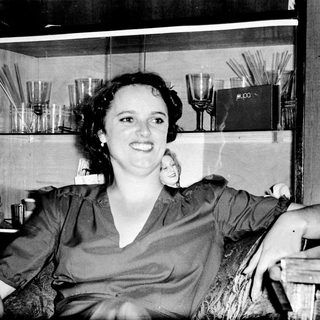 Woman smiling indoors near glass shelves with books.