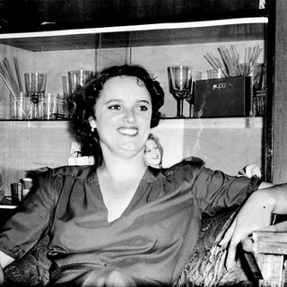 Woman smiling indoors near glass shelves with books.