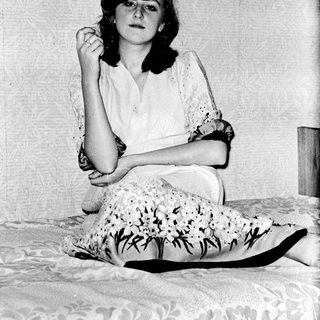 A woman sitting on a bed, adjusting her glasses.