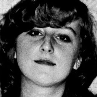 A woman sitting on a bed, adjusting her glasses.
